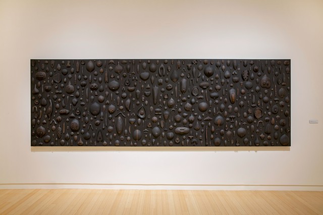 Biophilia (seeds) | black clay, graphite, pigment, sewing needles, wood panel | 60 x 180 x 2.5 inches