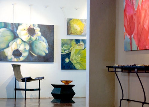Back room of gallery with small sling chair, square metal table and paintings of cactus and cactus flowers