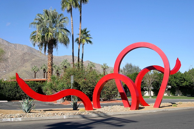 A monumental outdoor sculpture, "Jungle Red" is composed of large red fabricated steel beams that appears to move in and out of the ground in both a dramatic and whimsical style.
