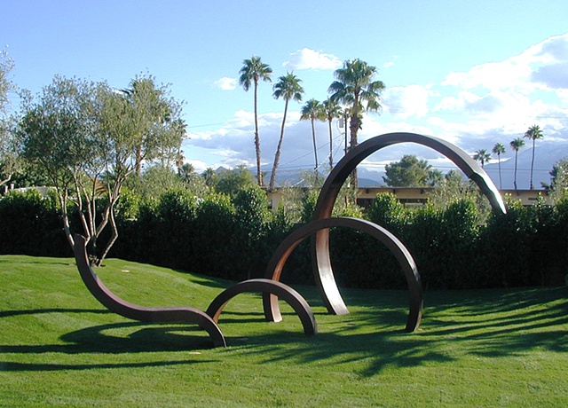 Large outdoor patinated steel sculpture that moves in and out of the ground in increasingly sized rings.  