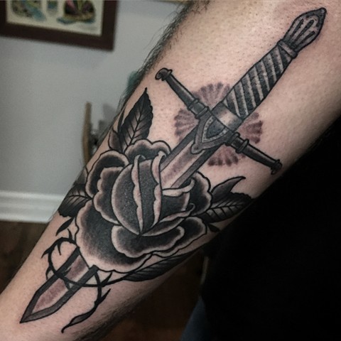 Scottish dagger through a classic black and grey rose tattoo on the arm, made in Toronto
