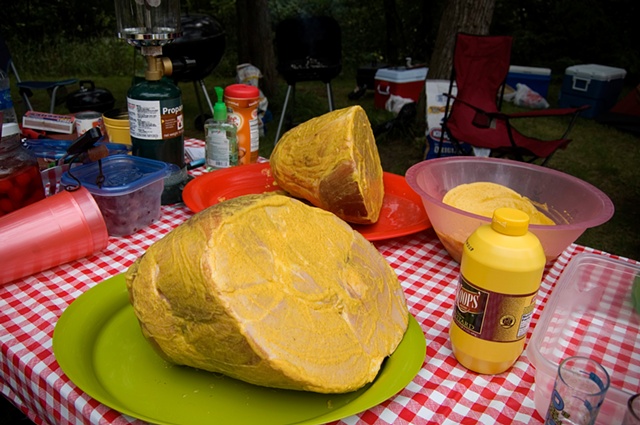 A ham slathered in mustard on a picnic table with red checked tablecloth by lucy Mueller