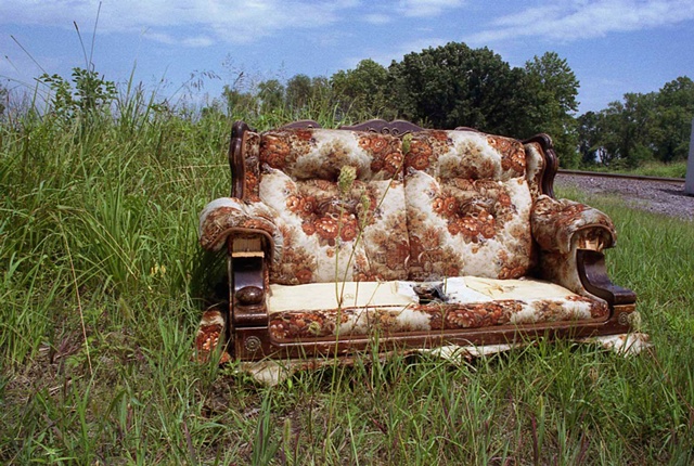 Abandoned orange and brown floral patterned couch abandoned by a railroad track by Lucy Mueller