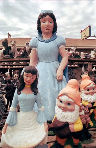 A Snow White concrete lawn sculpture with  a deformed unfinished mouth stands with her dwarfs in Mitchell, South Dakota photographed by lucy mueller 
