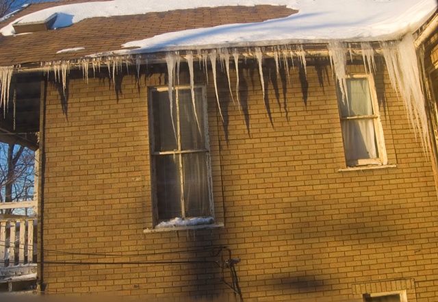 large icicles hang from the upstairs of an old house that is bathed in afternoon sun photographed by Lucy Mueller