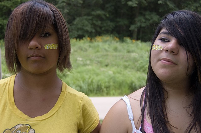 Two pubescent girls with colorful band aids on opposite cheeks by Lucy Mueller