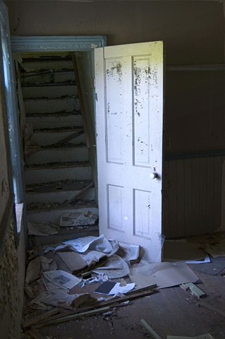 A door with peeling paint leading to a darkened staircase in an abandoned house by Lucy mueller