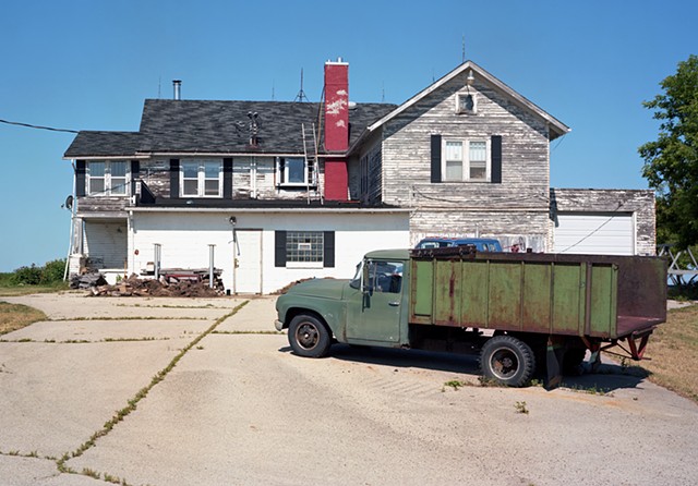 image of a white building with pealing paint, green truck in front with flat tire
