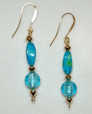 Earrings of faceted aqua glass bead with touches of green accompanied by an aqua murano style glass round bead accented with gold tone cone-shaped metal spacers 