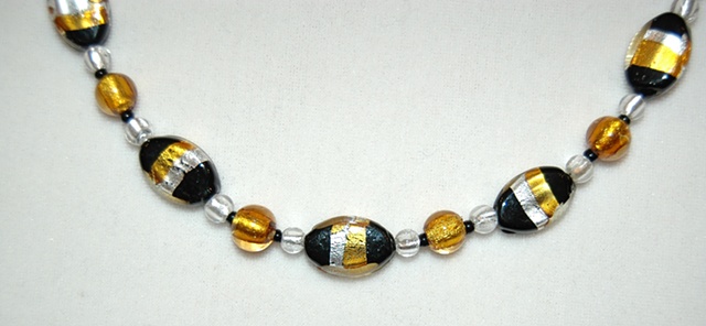 Necklace of black oval glass beads wrapped with silver and gold foil, with accent beads of round silver and gold murano style glass and black seed beads