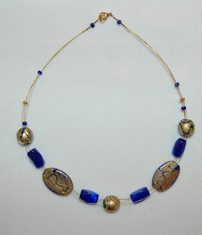 Triple strand necklace of interwoven incised gold foil over cobalt blue glass beads, oval and round in shape, accented with faceted cobalt blue glass
