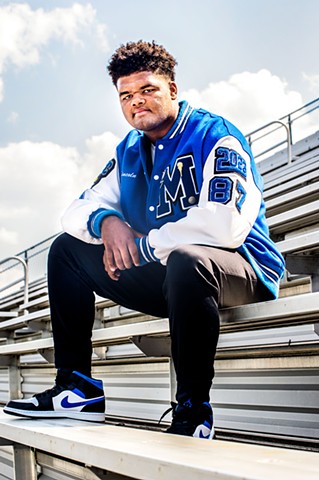 A portrait of high school senior, Lincoln who plays football. Lincoln sits on the football bleachers bench.