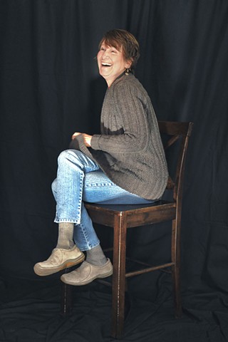 Portrait of veteran Lynne (laughing) who sits on a stool during volunteer event.
