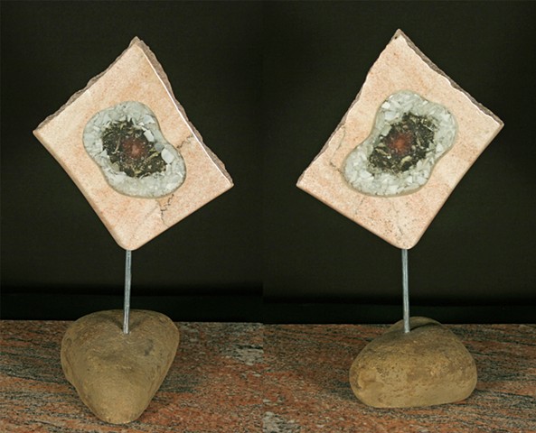 This mixed media sculpture consists of an open pink marble slab filled with glass shards and light sensitive frit encased in clear epoxy resin.  The form is suspended by a pin on a natural sandstone base.