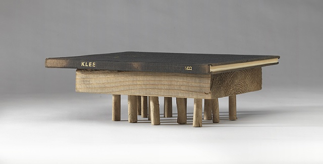 A book about the artist Paul Klee rests on a wooden block suported by numerous small legs.