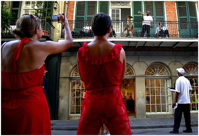 Participants of The Red Dress Run listen to music being performed on a balcony on Royal Street Dirty Linen Night.