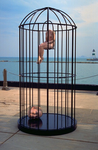 figurative polychrome sculpture of small body and large head in large steel bird-cage at Pier Walk Chicago