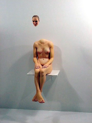 figurative polychrome sculpture which uses perspective to put a head on a headless bosy, smaller than life-size seated on a shelf