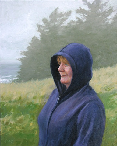 Woman in blue hooded sweatshirt, ocean and firs in foggy background.