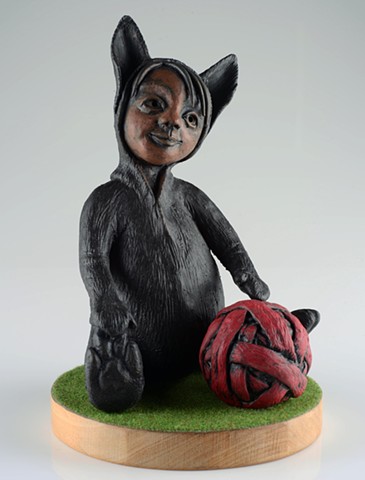 Child dressed in a black cat 'onesie', lightly touching a large ball of yarn as if about to play.