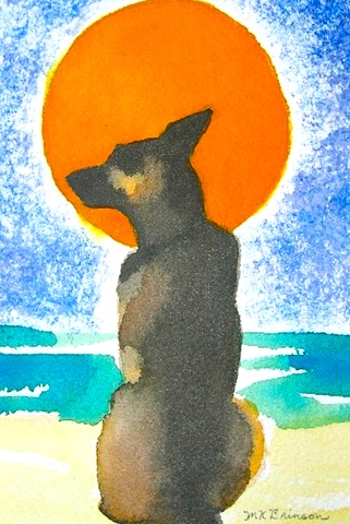 A German Shepherd dog sits on the beach before a big orange sun.