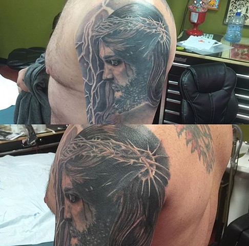 Jesus portrait tattoo in black and grey artwork on upper arm Strange World Tattoo Calgary, Canada
