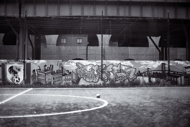 Photograph of a soccer ball in front of a graffiti covered wall along the Hudson River Greenway, Manhattan, New York, by Judith Ebenstein