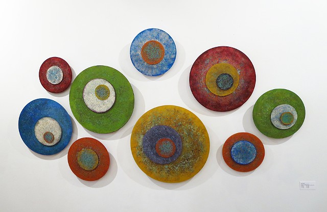 Wall sculpture installation of several circular paintings on acrylic panels.