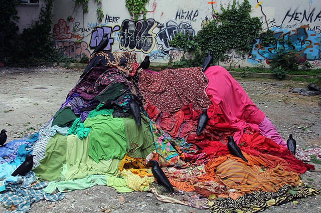 Art installation by artist Paul March, entitled Welcome to the Pleasure Dome, resembling crows on multicoloured pile of clothes in wasteland