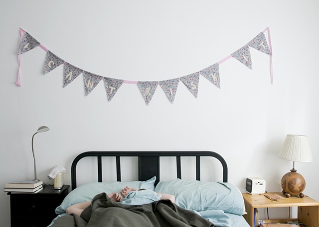 Bunting banner reading, "I can't risk it" hanging above figure in unmade bed.
