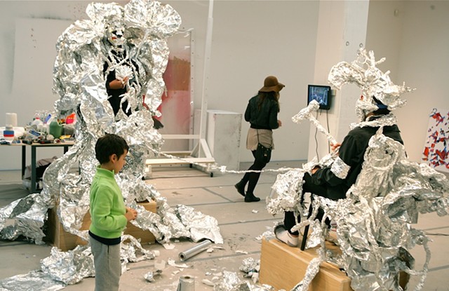 Two teenagers started out making aluminum foil mask to conceal themselves. Visitors were invited to further adorn the participant with aluminum foil (adding not subtracting).