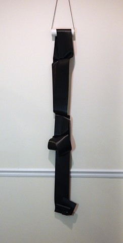 Contemporary, minimalist, wall mounted sculpture by Robert Fields, "Night nots/knots," 2019. Media: Vinyl sheet (black), metal clamps, PVC pipe, and nylon cord, 82 x 10 x 6 inches.