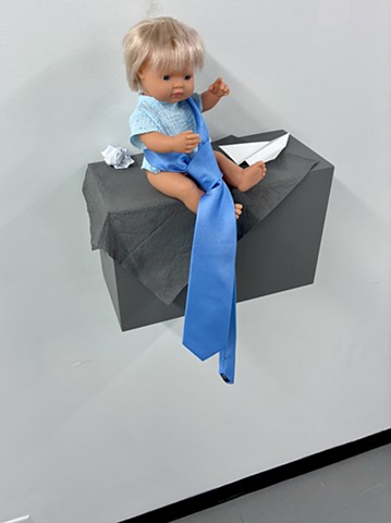 Conceptual Art, Socially Engaged Art, Robert Fields, UNTITLED (Whass PEE-WEE hiding? HUH? // 'Look. See. MY new plane.'), 2025. Bare-ass Baby Boy doll, men's dress-tie, with paper + latex paint on fiber and wood. Overall: 25" x 18" x 11". Doll: 12" x 6" x 8". Plinth: 10-1/2" x 16" x 7".