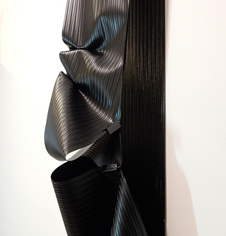 Contemporary, minimalist, wall mounted sculpture by Robert Fields, "Nocturnal River," 2019. Media: Vinyl sheet (black), metal clamps, PVC pipe, foam and nylon cord, 82 x 10 x 6 inches.