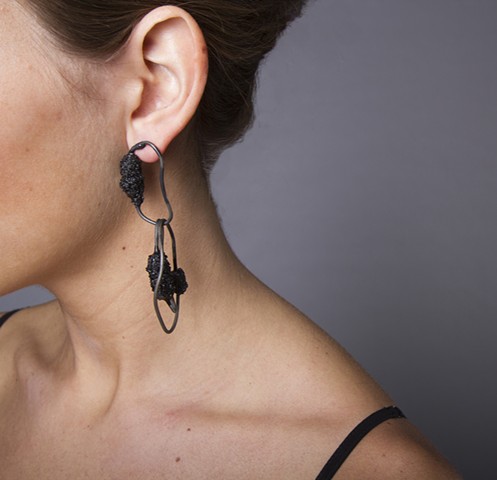 a one-of-a-kind pair of earrings that are composed of welded steel wire chain links and a handmade bead composed of broken black vine charcoal, powdered graphite, lacquer and plastic dip.