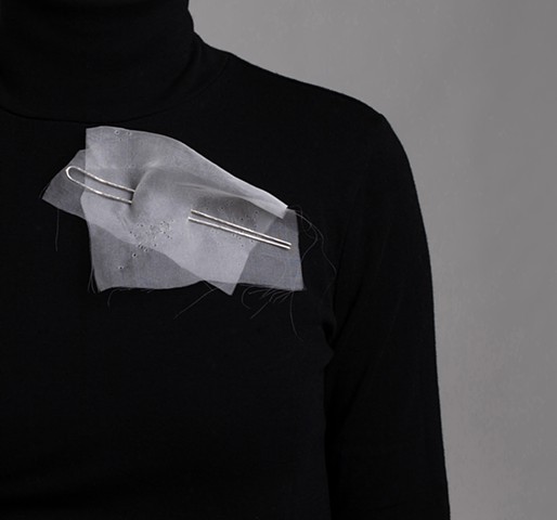 Through wearing, the delicate fabric records each act of pinning, leaving a visible collection of holes.