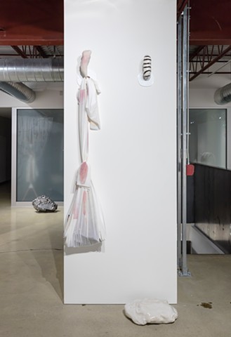 Installation view showing 'Really It's A Lot Bigger, A Lot Heavier, And A Lot Darker #18' and 'Bindle bundle v. 01 (with purple Doritos—Spicy Sweet Chili—poopy diaper/baby carried by stork/Liz Magor hoard) and some visual extrapolation—brown stripes, porc
