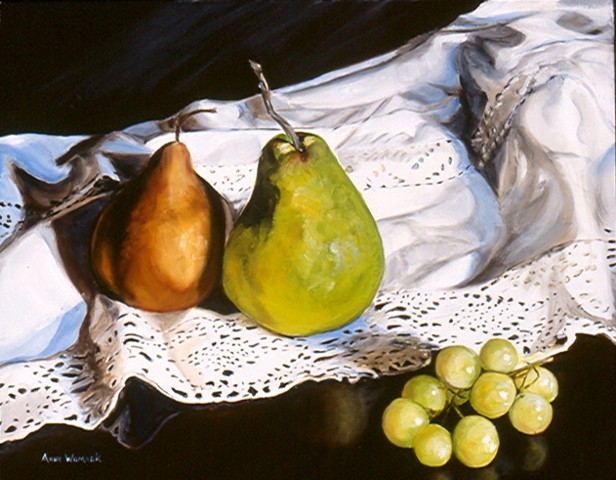 A brown and yellow pear both sit on a white cloth with lace.  Green grapes sit on a mahogany surface