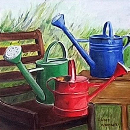 Green, Red, and Blue watering cans in a garden.  Brown chair and table