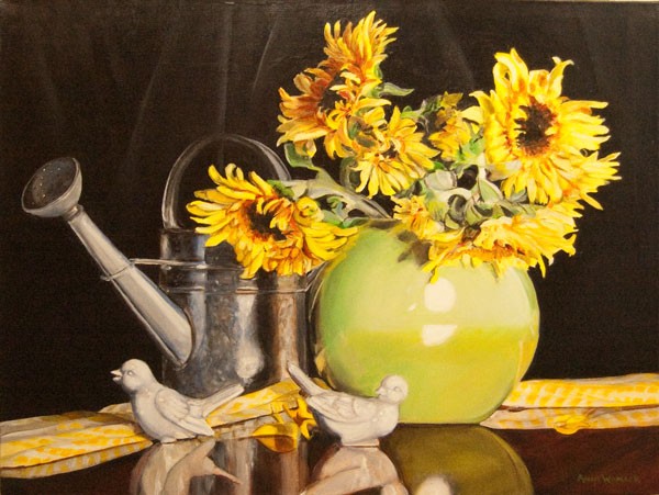 A galvanized watering can sits behind a lime green vase filled with sunflowers. The vase, two white porcelain birds and a yellow checked cloth reflect on the surface.  Colors pop against the black background.