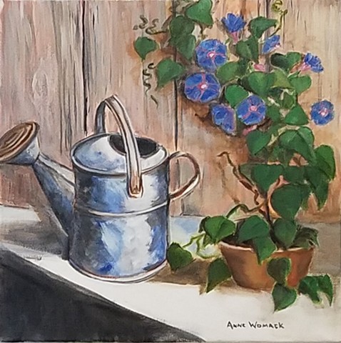 Metal watering can in front of a fence.  A morning glory vine grows on the fence