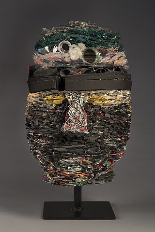 Head sculpture made with tightly layered recycled materials:  magazines, plastic bottles, pop cans, rubber, a toothpaste tube, etc. Suggests ideas about identity as packaged, or the result of the by-products of consumerism, and in need of renewal.