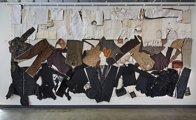 Assemblage on canvas with found objects: layered coloured clothes with altered labels, pills, shoes, handbags, books. Explores critiques stereotypes of identity, polarized black/white. Questions attitudes beliefs tied to ideas about race in North America.