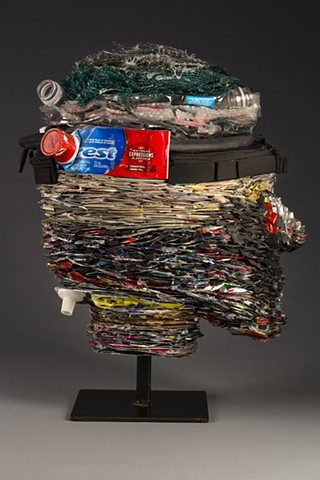 Head sculpture made with tightly layered recycled materials:  magazines, plastic bottles, pop cans, rubber, a toothpaste tube, etc. Suggests ideas about identity as packaged, or the result of the by-products of consumerism, and in need of renewal.