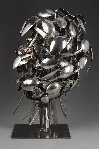 Sculpture made of metal spoons examines mixed black/white identity. Layered spoons covered with personal photos and race-related text references act of eating, feeding on or being fed information about one’s self and asks: How is identity constructed?