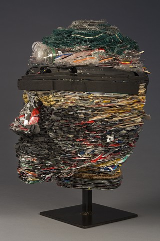 Head sculpture made with tightly layered recycled materials:  magazines, plastic bottles, pop cans, rubber, a toothpaste tube, etc. Suggests ideas about identity as packaged, or the result of the by-products of consumerism, and in need of renewal.