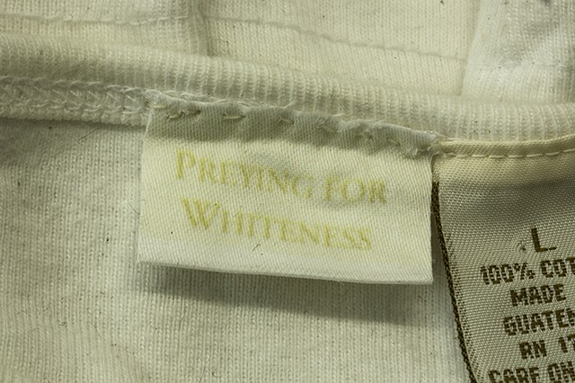 Assemblage on canvas with found objects: layered coloured clothes with altered labels, pills, shoes, handbags, books. Explores critiques stereotypes of identity, polarized black/white. Questions attitudes beliefs tied to ideas about race in North America.