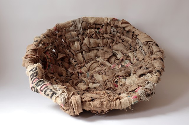 A large round textile comprised of woven strips of burlap coffee sacks into a papasan chair. The bottom right strip of burlap reads "Product". 
