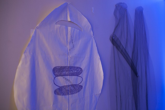 three cloth figures are pinned to the walls of a room illuminated by blue lights