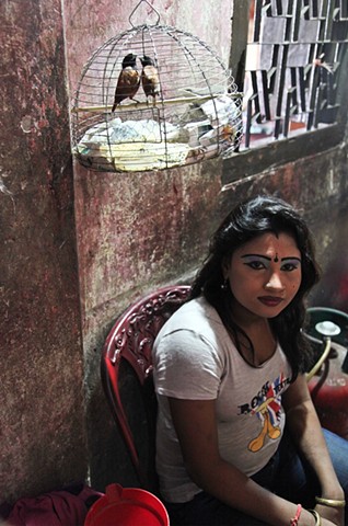 A young sex workers sits outside of her room with her pet birds at the Rathkhola Brothel in Faridpur, Bangladesh. The women put on elaborate makeup in the early afternoon to prepare for a long day of customers.